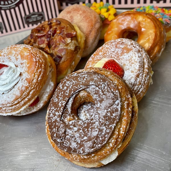 A close-up of various Mag's Donuts & Bakery cronuts, including chocolate, strawberry, and glazed.