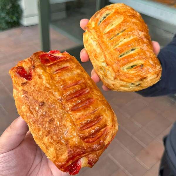 Two hands holding golden-brown pastries, one with red fruit filling and the other with dark filling.