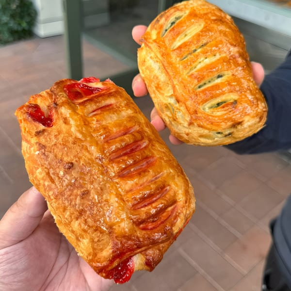 Two hands holding golden-brown pastries, one with red filling and the other with dark filling.
